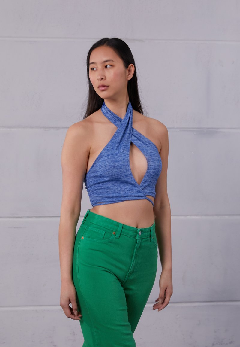 Top cropped azul com halter, com umDecote torcido e detalhe em gota, emparelhado com jeans verdes de cintura alta. Ambas as peças são ajustadas.