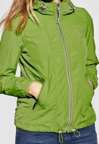 Zielona lekka kurtka z przodu na zamek błyskawiczny, regulowanym kapturem, dwiema bocznymi kieszeniami i elastycznym dołem. Gładki, teksturowany materiał z kontrastowymi detalami.