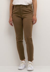 Brown, slim-fit pants with a smooth texture, mid-rise waist, and ankle-length design, paired with white sneakers.