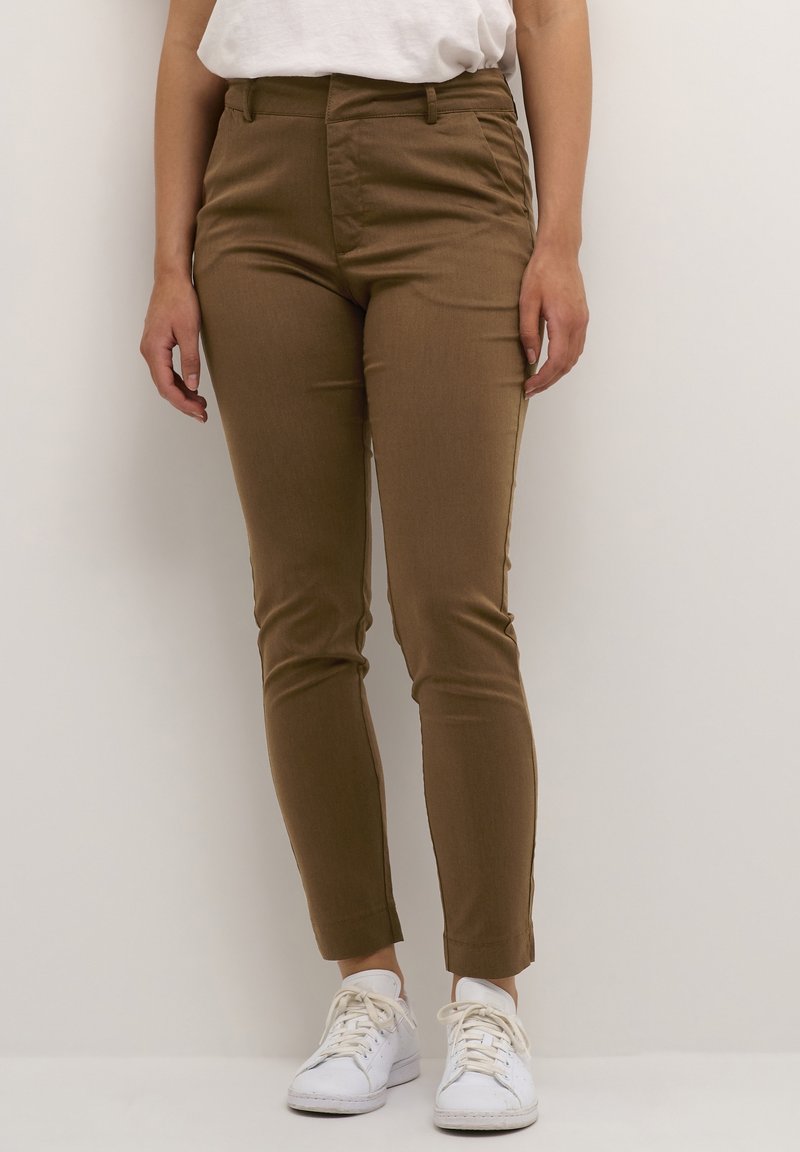 Brown, slim-fit pants with a smooth texture, mid-rise waist, and ankle-length design, paired with white sneakers.