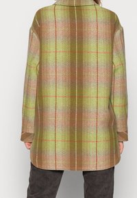 Uldblandingsfrakke i grøn, brun og beige plaid. Har krave, lange ærmer og en lige skæring med en let buet kant.