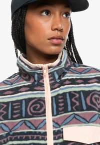 Fleece jacket featuring a zip-up front, high collar, abstract patterned design in dark blue, pink, and green with a light pink accent pocket.
