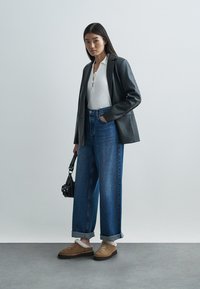 Czarna skórzana marynarka, biały prążkowany top, niebieskie dżinsy z wysokim stanem i szerokimi nogawkami, brązowe zamszowe buty z futrzanym ociepleniem oraz mała czarna torebka.