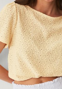 Gul cropped top med intrikate blomsterbroderier, med rund hals og korte ærmer, tekstureret stof med åbne mønstre.