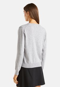 Světle šedý svetr s kulatým výstřihem a žebrovanými manžetami, vyrobený z měkké pleteniny. Má volný střih a jednoduchý design.