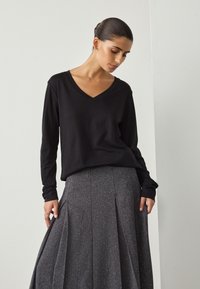 Czarna koszula z długim rękawem i dekoltem w serek, zestawiona z teksturowaną, błyszczącą szarą plisowaną spódnicą, charakteryzującą się klasyczną sylwetką i subtelnym blaskiem.