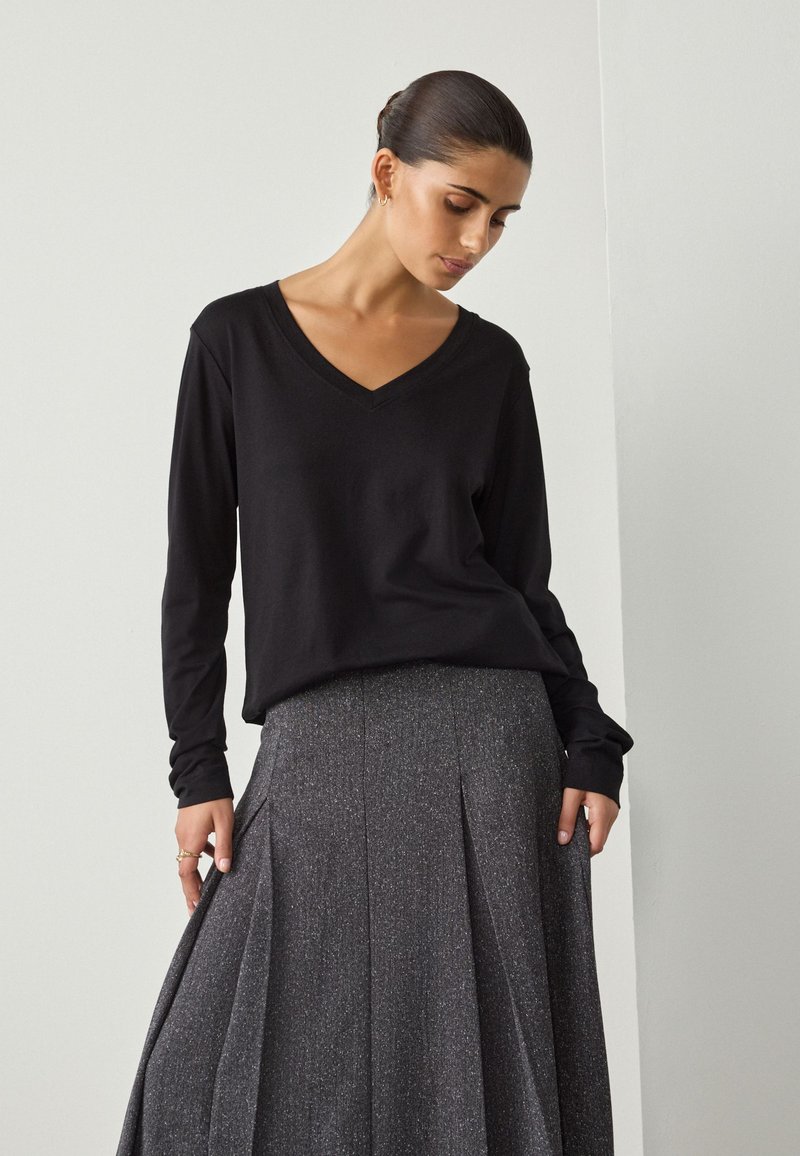 Czarna koszula z długim rękawem i dekoltem w serek, zestawiona z teksturowaną, błyszczącą szarą plisowaną spódnicą, charakteryzującą się klasyczną sylwetką i subtelnym blaskiem.