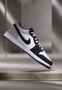 Nike edzőcipők, melyek fehér, fekete és szürke bőr kombinációjával rendelkeznek. Alacsony szárú kialakítás, texturált talppal és ikonikus swoosh logóval.