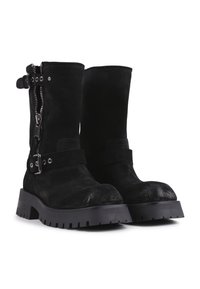 Botine negre din suede, cu fermoare pe lateral, accente metalice și talpă robustă din cauciuc. Prezintă un detaliu cu curea și cataramă lângă gleznă.