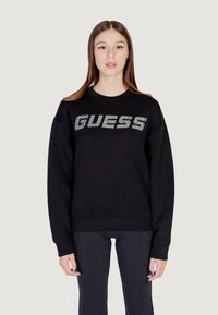 Čierna mikina s okrúhlym výstrihom, na ktorej je v striebornom trblietavom písmene napísané "GUESS", s voľným strihom a rebrovanými manžetami.