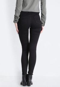 Svarta skinny jeans med hög midja, med bakfickor och ett mjukt, stretching tyg. Matchas med svarta ankelboots.