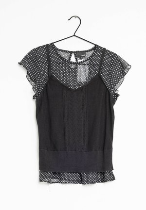 Top negro con mangas transparentes de lunares y un panel frontal de punto intrincado. Presenta un dobladillo con volantes y un cierre trasero con abertura en forma de llave.