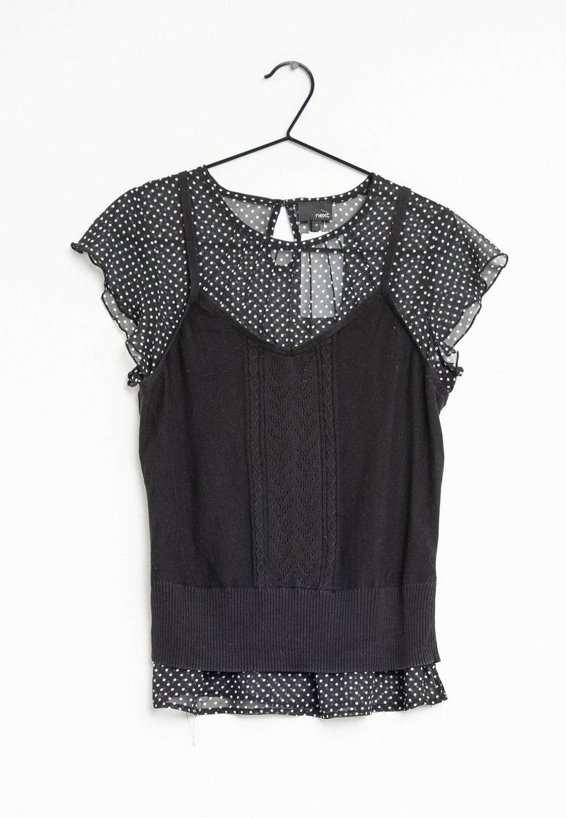 Haut noir avec manches en voile à pois et un panneau avant en tricot complexe. Comprend un ourlet à volants et une fermeture arrière avec ouverture en forme de trou de serrure.