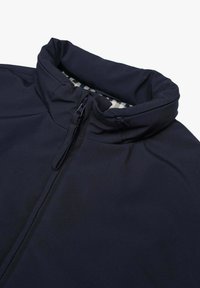 Giacca blu navy con colletto alto, chiusura a mezza zip e texture morbida; l'interno presenta un motivo a quadretti in colori chiari.