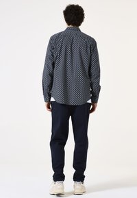 Camisa de botones en azul marino con un patrón circular, combinada con pantalones oscuros y zapatillas claras. Presenta un cuello estándar y mangas largas.