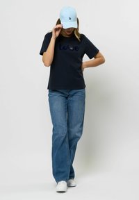 Mornarski majica s tekstom "ljubav", modra kapa, plave traper hlače i bijele tenisice. Kapa ima mali logo. Ukupno ležerna odjeća.