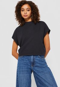 Schwarzes, kurzes T-Shirt mit umgeschlagenen kurzen Ärmeln, aus weichem Stoff, kombiniert mit blauen weiten Jeans im klassischen Fünf-Taschen-Design.