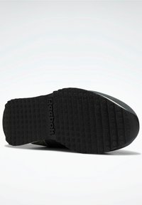 Semelle de chaussure Reebok noire avec des motifs de bande de roulement rectangulaires et le logo Reebok embossé au centre sur un fond blanc.