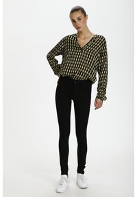 Langärmliges Hemd mit einem geometrischen Muster in Schwarz und Gold, kombiniert mit eng anliegenden schwarzen Hosen und weißen Sneakers. Flacher Schnitt und bequeme Passform.