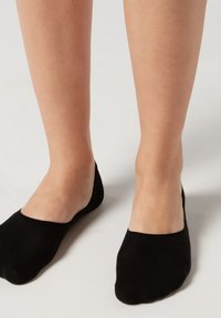 Schwarze Knöchelsocken aus einem weichen Material, die eng anliegen und einen niedrigen Schnitt haben. Sie verfügen über eine glatte Textur und einen nahtlosen Zehenbereich.