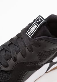 Černá atletická bota s texturovanou kůží a síťovaným svrškem, s tkaničkami, značkovou visačkou na jazyku a bílou gumovou podrážkou.