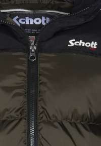 Chaqueta acolchada con cremallera en negro y verde olivo con textura de acolchado. Presenta el logotipo "Schott NYC" en blanco y rojo en la parte superior izquierda.