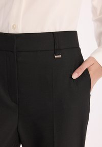 Czarne spodnie wykonane z teksturowanej tkaniny, z eleganckim pasem w talii z metalowym akcentem w kolorze srebrnym oraz bocznymi kieszeniami.