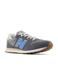 Scarpa atletica grigia con accenti blu, realizzata in rete e camoscio, punta rotonda, lacci bianchi e suola in gomma marrone chiaro.