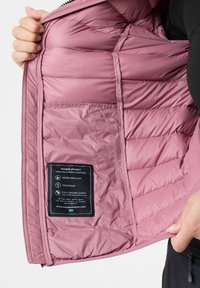 Indvendig af en nedjakke i blød pink, med quiltet isolering, en lomme med klap og et mærke med plejeanvisninger, vandafvisende og vindbeskyttende.