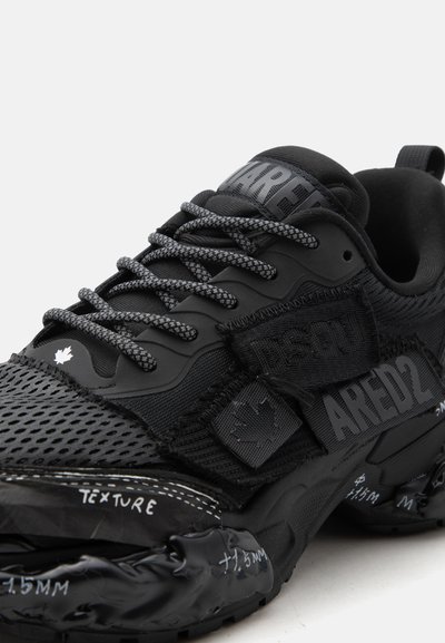 Μαύρο αθλητικό παπούτσι με ανάγλυφο επάνω μέρος από δίχτυ, γκρίζα κορδόνια με μοτίβο, ιμάντα με βέλκρο και εκτυπωμένες λεπτομέρειες κειμένου στη σόλα και στα πλαϊνά πάνελ.