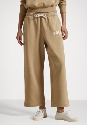 Beige, weite Sweatpants mit Kordelzugbund und weißem "POLO"-Logo. Weicher Stoff mit glatter Textur. Kombiniert mit hellen Sneakers.
