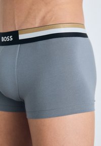Gray stretch fabric boxer briefs with a black waistband featuring gold and white striped accents and the brand name "BOSS" in white.
