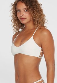 Biely trojuholníkový bikiny top s tenkými ramienkami a bočnými výrezmi, pričom má hladkú textúru a minimalistický dizajn.