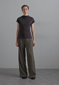 Dark, fitted top with a high neck and short sleeves paired with wide, high-waisted, olive-green trousers. Flat black shoes.