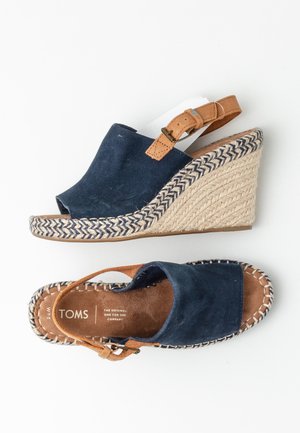 Sandales compensées en daim bleu marine avec une sangle en cuir marron à boucle et des détails en corde tressée le long de la semelle et du bord de la semelle intérieure.
