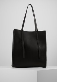 Zwarte leren tote bag met een gladde textuur, een langwerpige vorm en twee dunne handvatten. Minimalistisch ontwerp zonder externe hardware of patronen.