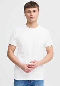 Hvid bomulds t-shirt med rund halsudskæring og korte ærmer, vist på en model foran en neutral baggrund. Enkelt og tætsiddende design.