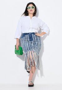 Gonna di denim con strisce frangiate bianche, abbinata a una maglietta bianca larga. Gli accessori includono una borsa verde e occhiali da sole color menta.
