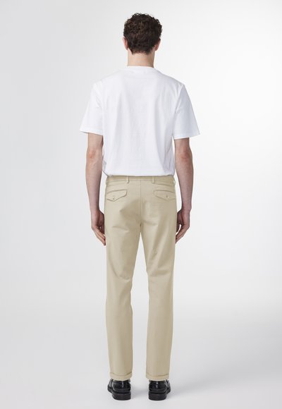 Hvid bomulds-t-shirt og beige lige ben bukser med baglommer; iført sorte sko; glat tekstur; minimalistisk design.