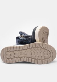 Botine din piele patent albastră, cu o suprafață texturată, având o talpă din cauciuc negru și crem, închidere cu fermoar și un model de banda proeminent.