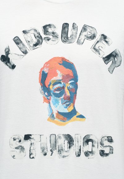 Λευκό βαμβακερό t-shirt με πολύχρωμο έργο τέχνης ενός προσώπου και έντονο κείμενο που γράφει «KIDSUPER STUDIOS» σε μαύρο και γκρι.