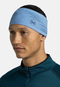 Diadema de poliéster azul claro con un diseño texturizado y un logo sutil. Combinada con una sudadera con cremallera en verde azulado, resaltando su estilo atlético.
