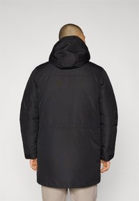 Chaqueta negra acolchada con capucha, de diseño de longitud media, puños elásticos y textura suave. Estilo simple y funcional.