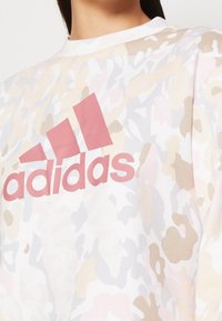 Felpa bianca con motivo mimetico pastello e grande logo rosa "adidas" al centro del petto. Tessuto morbido al tatto.