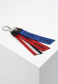 Portachiavi Tommy Jeans con tre strisce di tessuto in blu, rosso e nero con la scritta "TOMMY JEANS", attaccato a un anello portachiavi in metallo argento.