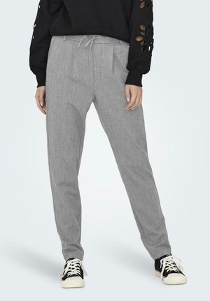 Graue Hose mit strukturiertem Muster, ausgestattet mit einem Kordelzugbund und Falten. Getragen mit einem schwarzen Oberteil und schwarz-weißen Sneakers.