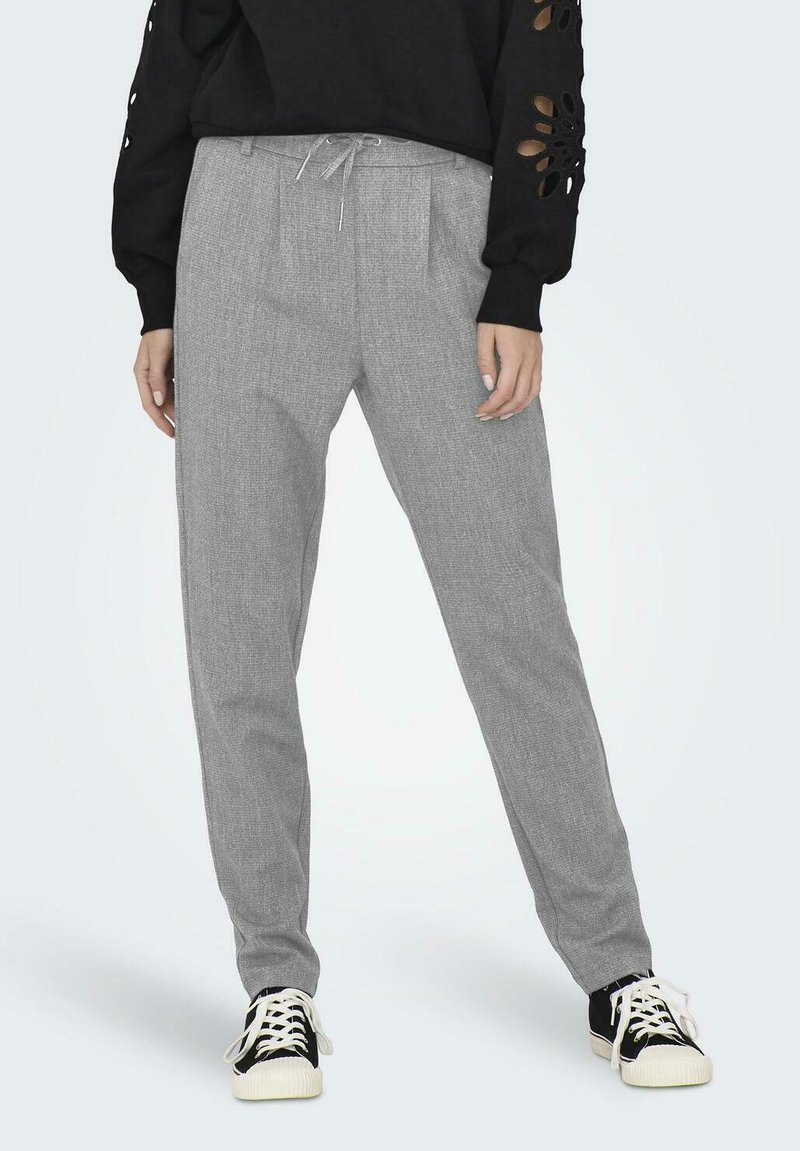 Graue Hose mit strukturiertem Muster, ausgestattet mit einem Kordelzugbund und Falten. Getragen mit einem schwarzen Oberteil und schwarz-weißen Sneakers.