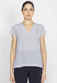 Bluzka z dekoltem w serek z lekkiego materiału, z białym tłem i niebieskim abstrakcyjnym wzorem, krótkimi rękawami oraz luźnym krojem u dołu.