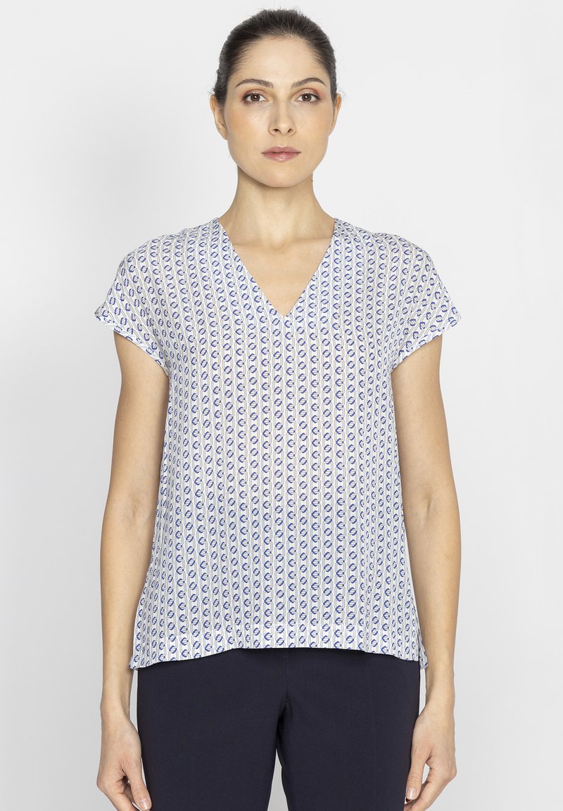 Bluzka z dekoltem w serek z lekkiego materiału, z białym tłem i niebieskim abstrakcyjnym wzorem, krótkimi rękawami oraz luźnym krojem u dołu.