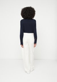 Tmavomodrá košeľa s dlhými rukávmi a gombíkmi na manžetách, skombinovaná s bielymi nohavicami s vysokým pásom a širokými nohavicami so zadnými vreckami. Jednoduchý a moderný dizajn.